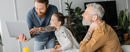 Homosexual parents with laptop helping smiling daughter doing homework at home, banner 