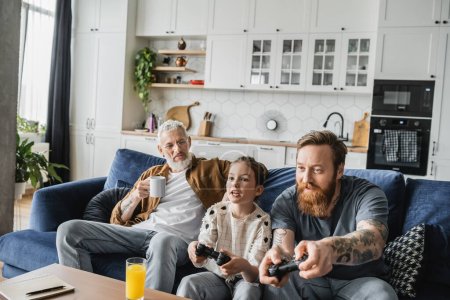 Photo for KYIV, UKRAINE - APRIL 19, 2023: Homosexual man playing video game with preteen daughter near partner at home - Royalty Free Image