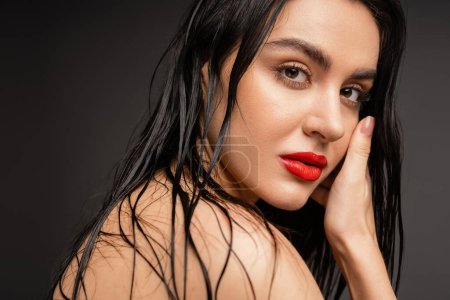 Photo for Young and charming woman with wet brunette hair and red lips posing with bare shoulders while looking at camera after shower isolated on grey background - Royalty Free Image