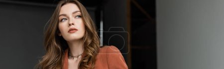 Photo for Portrait of brunette young woman with long hair and necklace wearing terracotta blazer and looking away on grey background in studio, sophisticated lady, banner - Royalty Free Image