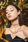 asian young woman with short hair posing in strapless dress with black glove while standing next to shiny yellow background, model, looking away, wrinkled golden foil, wet hairstyle  Poster #658081320