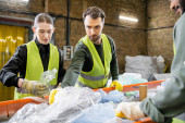 Male worker in protective vest taking plastic from conveyor while working near interracial colleagues in blurred garbage sorting center, garbage sorting and recycling concept Sweatshirt #658269204