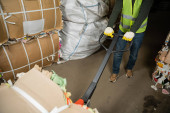 Cropped view of sorter in high visibility vest and gloves using hand pallet truck and moving waste paper in garbage sorting center, waste sorting and recycling concept Stickers #658270200