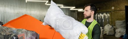 Photo for Side view of bearded man in protective vest and glove putting sack with trash in container while working in waste disposal station, garbage sorting and recycling concept, banner - Royalty Free Image