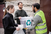Smiling volunteers giving trash to indian worker in high visibility vest in outdoor waste disposal station, garbage sorting and recycling concept Longsleeve T-shirt #658271750