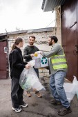 Smiling indian worker in protective vest taking trash from volunteers near door of waste disposal station outdoors, garbage sorting and recycling concept Longsleeve T-shirt #658271774