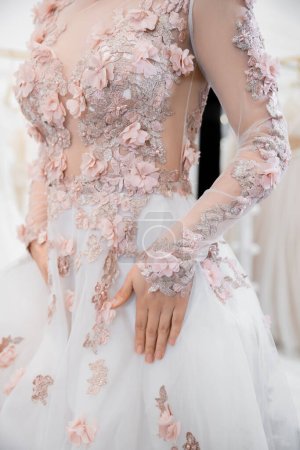 Ausgeschnittene Ansicht einer Frau, die in einem wunderschönen und floralen Hochzeitskleid in einem luxuriösen Salon um verschwommene weiße Tüll-Stoffe steht, Brauteinkäufe, zukünftige Braut, Details, Vorbereitung für einen besonderen Tag 
