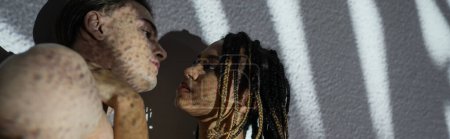 low angle view of attractive and seductive african american woman with stylish dreadlocks standing near sexy shirtless man on white textured background with grey shadows, banner