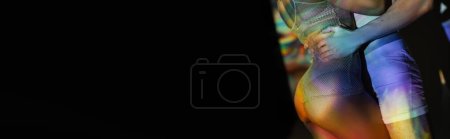 vista parcial del hombre en calzoncillos abrazando a la mujer afroamericana con nalgas sexy, en un elegante traje de red en el fondo con efectos de iluminación de colores y espacio de copia negro, pancarta 