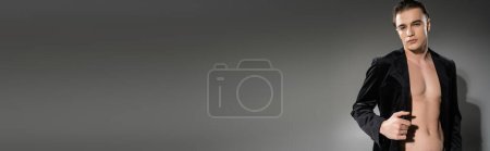 Photo for Young, handsome and fashionable man with brunette hair, wearing black silk blazer on shirtless body, posing and looking at camera on grey background, banner - Royalty Free Image