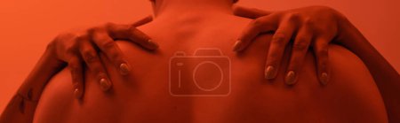 Foto de Vista recortada de hombre masculino sin camisa con el cuerpo muscular cerca apasionada mujer afroamericana abrazándolo sobre fondo naranja con efecto de iluminación roja, bandera - Imagen libre de derechos