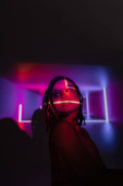 portrait of youthful and impassioned african american woman with dreadlocks looking away while standing on abstract black and purple background with neon rays and lighting effects Mouse Pad 658777540