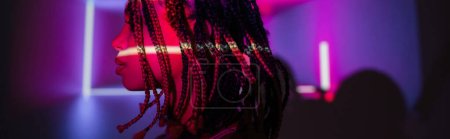 Photo for Profile of young and captivating african american woman with dreadlocks posing on abstract purple background with radiant neon rays and lighting effects, banner - Royalty Free Image