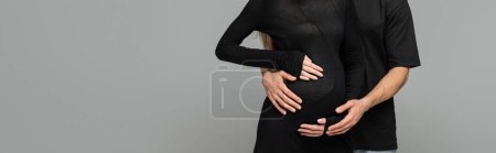 Cropped view of man in black t-shirt hugging stylish pregnant wife in dress while standing together isolated on grey with copy space, new beginnings and anticipation concept, banner 