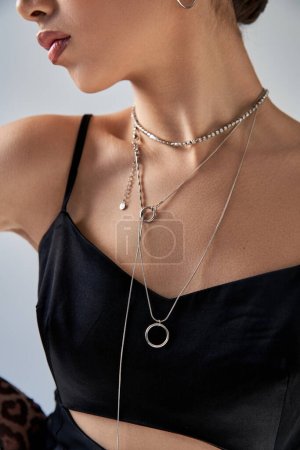Photo for Cropped view of young and fashionable woman in silver necklaces, black and elegant strap dress standing on grey background, spring fashion photography, generation z - Royalty Free Image