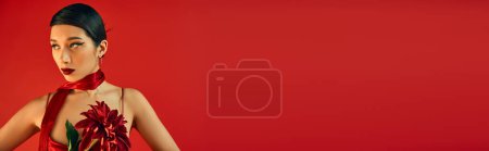 gen z fashion, Spring style, Porträt einer ausdrucksstarken asiatischen Frau in hellem Halstuch, mit brünetten Haaren und kühnem Make-up, die in der Nähe einer weinroten Pfingstrose auf rotem Hintergrund wegschaut, Banner