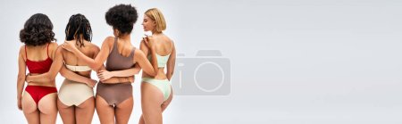 Photo for Smiling young woman in colorful lingerie hugging multiethnic friends while posing together isolated on grey, different body types and self-acceptance concept, multicultural representation, banner - Royalty Free Image