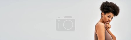 Photo for Portrait of confident african american woman in brown lingerie touching chin and looking at camera while standing isolated on grey, self-acceptance and body positive concept, banner - Royalty Free Image