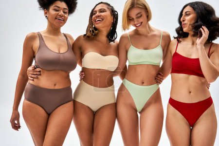 Photo for Confident and sexy multiethnic women in colorful lingerie hugging each other while posing and standing isolated on grey, different body types and self-acceptance, multicultural representation - Royalty Free Image