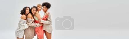Joyful multiethnic girlfriends in stylish and knitted sweaters hugging each other isolated on grey, different body types and self-acceptance, multicultural representation, banner with copy space