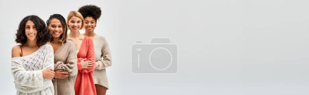 Photo for Positive and multiethnic girlfriends in stylish warm sweaters crossing arms while posing and standing isolated on grey, different body types and self-acceptance, multicultural representation, banner - Royalty Free Image