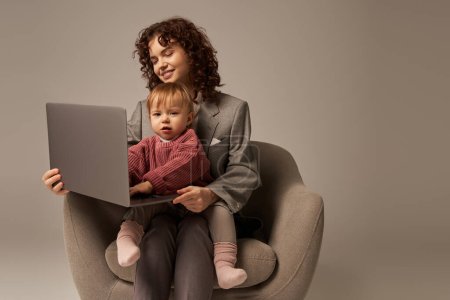 building successful career, work life success, working parent, happy businesswoman using laptop and sitting on armchair with daughter, mother and child, motherhood, multitasking 