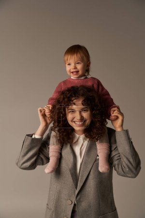motherhood, work life balance, cheerful working mother with kid on shoulders, woman and happy daughter on grey background, work life harmony concept, loving motherhood, quality family time 