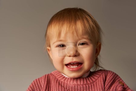 Portrait von niedlichen Baby-Mädchen, Kleinkind, glückliches kleines Kind in lässiger Kleidung lächelnd auf grauem Hintergrund im Studio, Emotionen, Unschuld, Kleinkind-Mode, stilvolles Outfit, rosa Pullover, Babygesicht