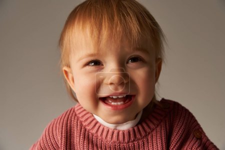 Porträt eines süßen Mädchens, eines Kleinkindes, eines kleinen Kindes in lässiger Kleidung, das im Studio auf grauen Hintergrund in die Kamera blickt, Emotionen, Unschuld, Kleinkindmode, stylisches Outfit, Pullover, Glück 