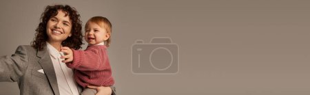 Photo for Career and family, motherhood, quality family time, happy and curly woman holding in arms toddler daughter on grey background, balancing between work and life, positivity, banner - Royalty Free Image