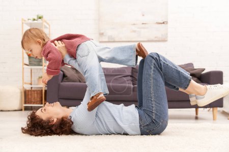 quality family time, happy mother lifting toddler daughter and lying on carpet in cozy living room, work life balance, denim clothes, casual attire, family relationships, modern parenting 