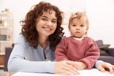 portrait of happy woman and child, curly working mother hugging baby girl, balanced lifestyle, bonding, family time, modern parenting, engaging with kid, loving motherhood 