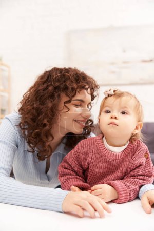 portrait of cheerful woman and child, curly working mother hugging baby girl, balanced lifestyle, bonding, happy family time, modern parenting, engaging with kid, loving motherhood 