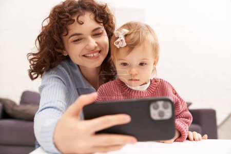 Selfie, moderne Elternschaft, fröhliche Frau beim Selfie mit Baby-Mädchen, Smartphone, Kleinkind und lockige Mutter, Porträt, digitales Zeitalter, Familienbeziehungen, Umgang mit Kind, Qualitätszeit 