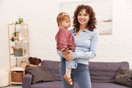 balanced lifestyle, working mother with curly hair holding in arms baby girl, woman and her toddler daughter, modern parenting, work life harmony, bonding and engaging with kid, happiness 