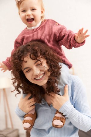Foto de Mujer alegre con la muchacha feliz del bebé en hombros, estilo de vida equilibrado, tiempo de la hija de la mamá, divertirse juntos, tiempo de calidad, trabajo y armonía de la vida, maternidad cariñosa, felicidad - Imagen libre de derechos