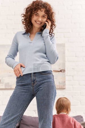 cheerful young woman talking on smartphone standing near toddler kid, balancing between work and life, modern parenting, remote work, career and family, casual attire 