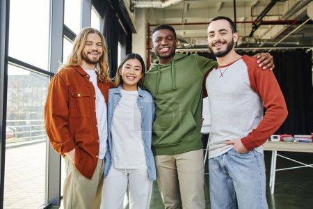 african american man embracing overjoyed interracial friends in stylish casual clothes looking at camera in modern office, diverse team business collaboration, startup project, entrepreneurship