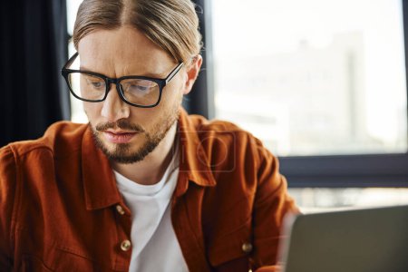 portrait of thoughtful entrepreneur in eyeglasses and trendy shirt thinking in contemporary office, business lifestyle, professional development, working on startup project