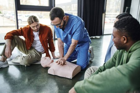 professionelle Gesundheitsfachkraft macht Brustkompressionen an CPR-Schaufensterpuppen und zeigt jungen multiethnischen Teilnehmern des Erste-Hilfe-Seminars im Schulungsraum Herz-Lungen-Wiederbelebung