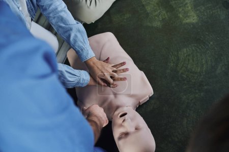 first aid seminar, top view of young woman practicing life-saving skills while doing chest compressions on CPR manikin near medical instructor, emergency situations response concept, cropped view