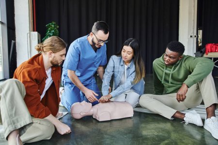 young asian woman practicing life-saving skills by doing chest compressions on CPR manikin near multiethnic team and medical instructor, cardiopulmonary resuscitation, first aid training seminar