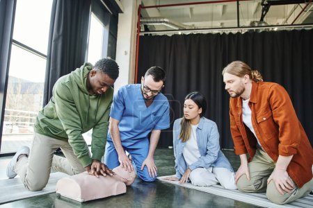 Afrikanisch-amerikanischer Mann macht Brustkompressionen an CPR-Schaufensterpuppe während des praktischen Lernens auf einem Erste-Hilfe-Seminar in der Nähe professioneller Sanitäter und einer vielfältigen Gruppe junger multiethnischer Teilnehmer