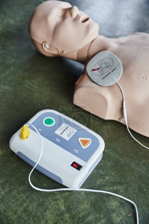 Hochwinkelaufnahme des automatisierten externen Defibrillators in der Nähe der Herz-Lungen-Wiederbelebungsmanikin des Fußbodens im Schulungsraum, medizinisches Gerät für Erste-Hilfe-Schulungen und Kompetenzentwicklung