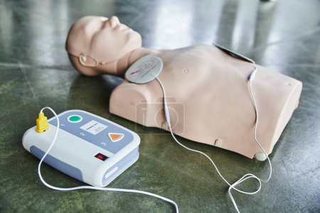selektive Fokussierung des automatisierten externen Defibrillators in der Nähe von Herz-Lungen-Wiederbelebungsübungen auf verschwommenem Hintergrund auf dem Boden im Schulungsraum, medizinische Ausrüstung für Erste-Hilfe-Schulungen 