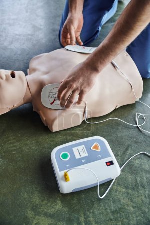 cardiac resuscitation techniques, partial view of professional paramedic applying defibrillator pads on CPR manikin, high angle view, health care and life-saving techniques concept