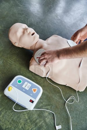 Ausgeschnittene Ansicht des professionellen Gesundheitspersonals, das Defibrillator-Pads auf CPR-Schaufensterpuppe, Herz-Wiederbelebung, Hochwinkel-Ansicht, Gesundheitsfürsorge und lebensrettende Techniken anwendet