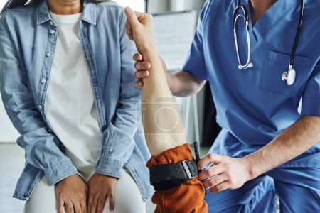 vue recadrée d'un ambulancier paramédical professionnel appliquant un garrot de compression sur le bras d'un homme près d'une jeune femme lors d'un séminaire de premiers soins en salle d'entraînement, concept de réponse aux situations d'urgence
