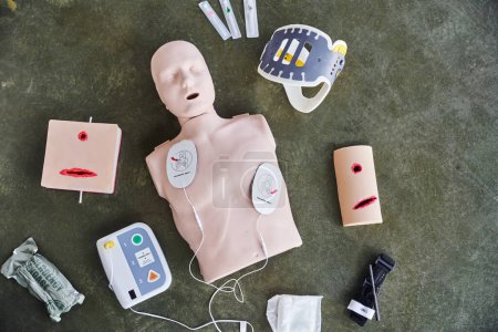 top view of CPR manikin, automated external defibrillator, wound care simulators, neck brace, syringes, compression tourniquet and bandage, medical equipment for first aid training 