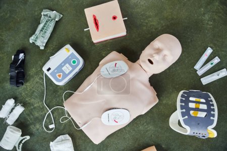 top view of CPR manikin, automated external defibrillator, wound care simulator, neck brace, bandages, syringes and compression tourniquet, medical equipment for first aid training